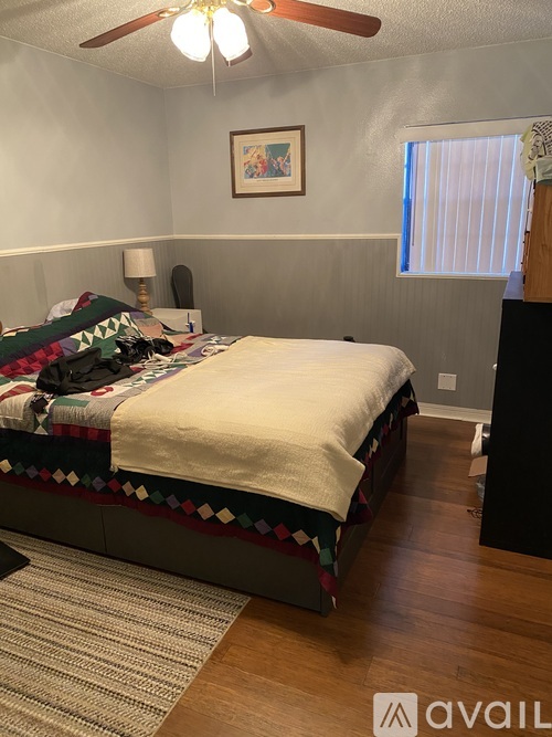 A bedroom with a bed, a ceiling fan, and a picture on the wall.