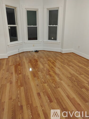 A room with wooden flooring and three windows.