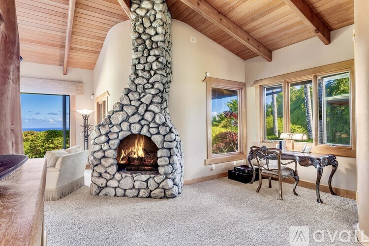 A stone fireplace is in the middle of a living room with a couch and chairs.