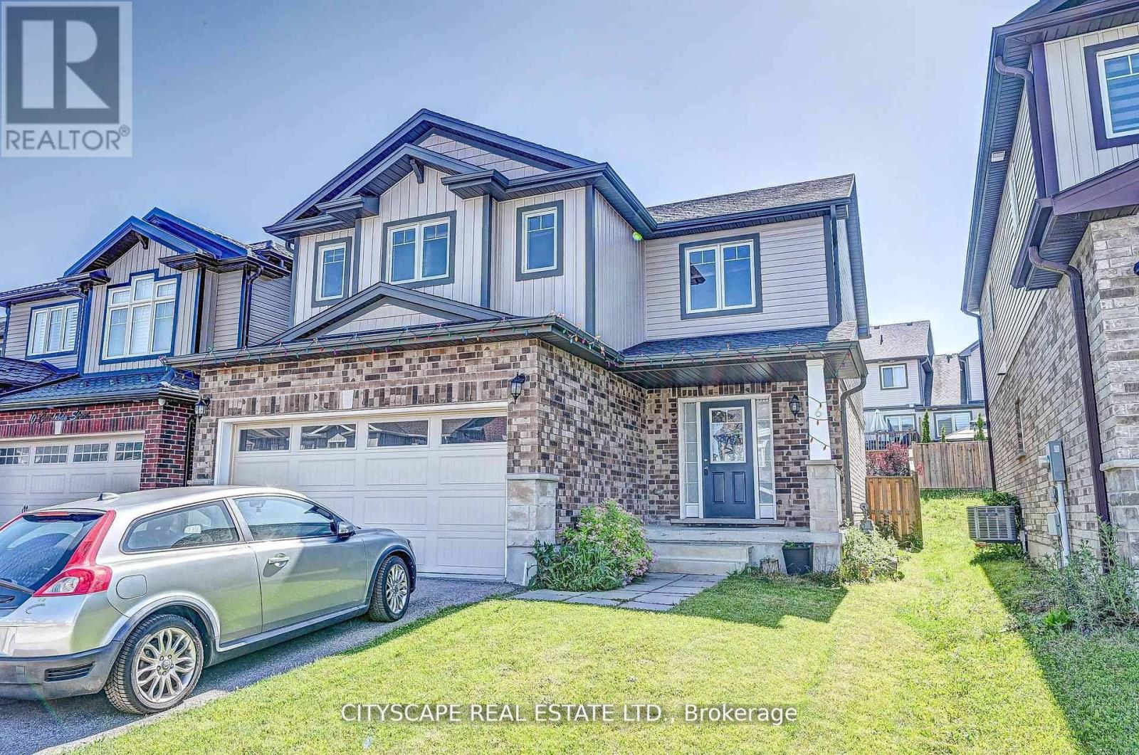 A grey car is parked in front of a house with a stone wall.