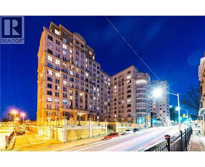 A nighttime city street with a tall building on the left and cars driving by.