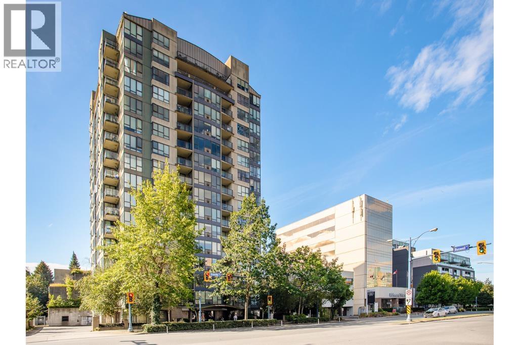 A tall building with many windows is in the foreground of a city street.