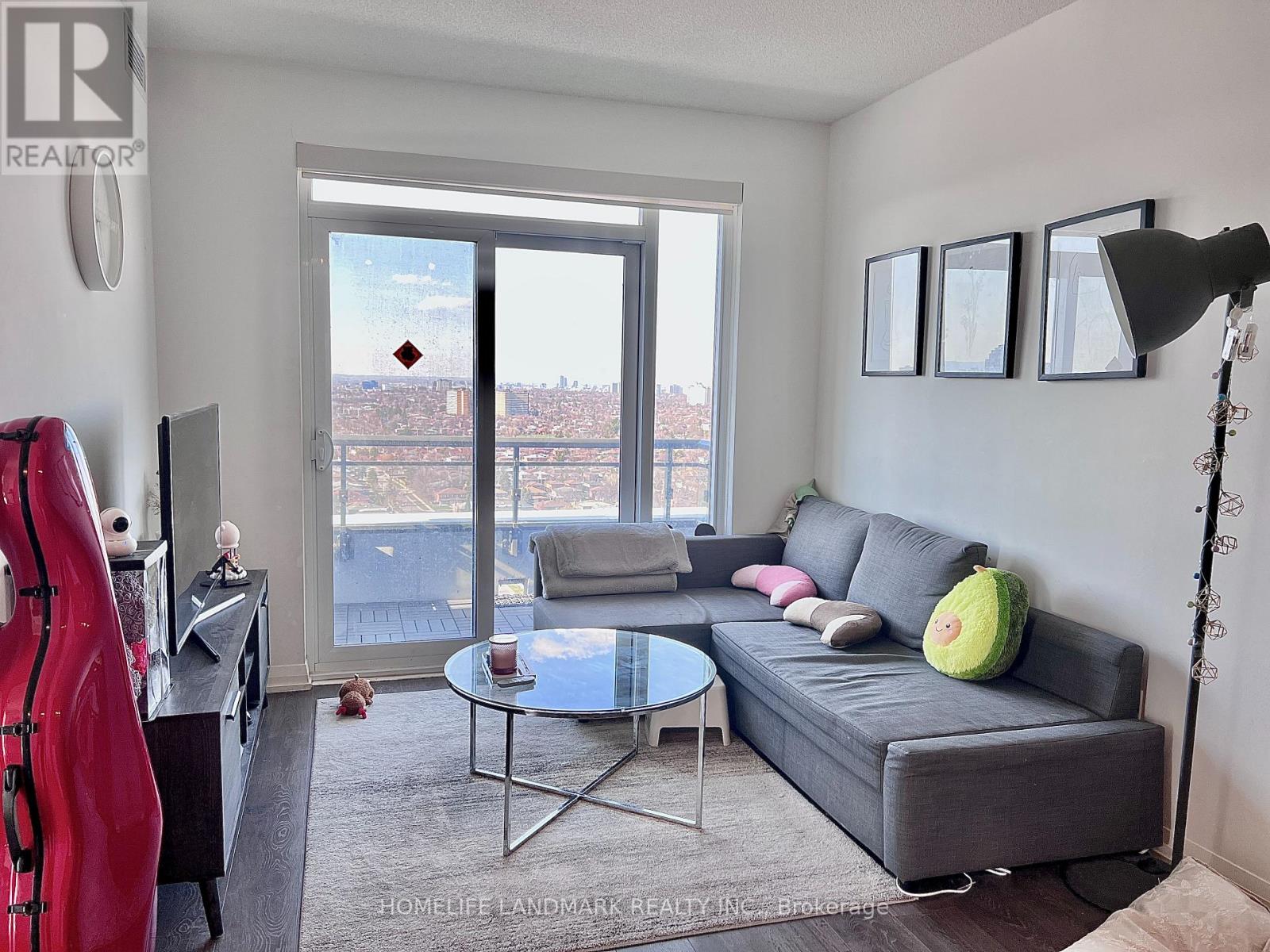 A living room with a grey couch, a glass table, a red sculpture, and a view of the city through the window.