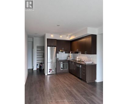 A modern kitchen with dark wood floors and stainless steel appliances.