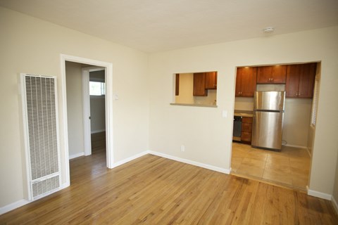 an empty living room with wood floors and a kitchen