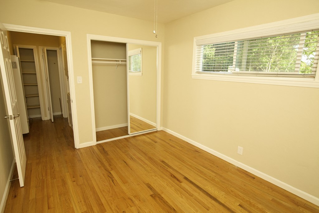 an empty room with wooden floors and a closet and a window