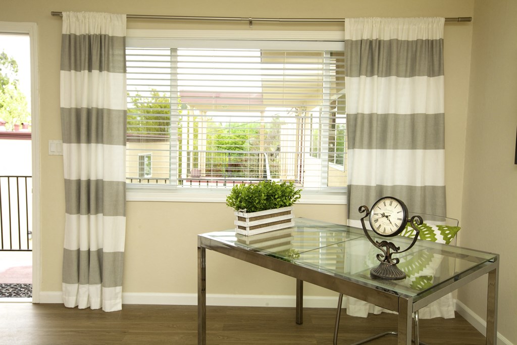 a living room with a glass table and window with striped curtains