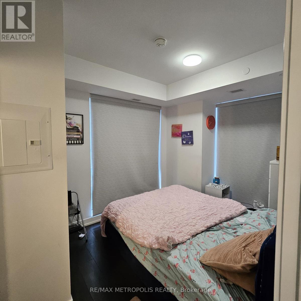 A bedroom with a bed, a nightstand, and a window with blinds.