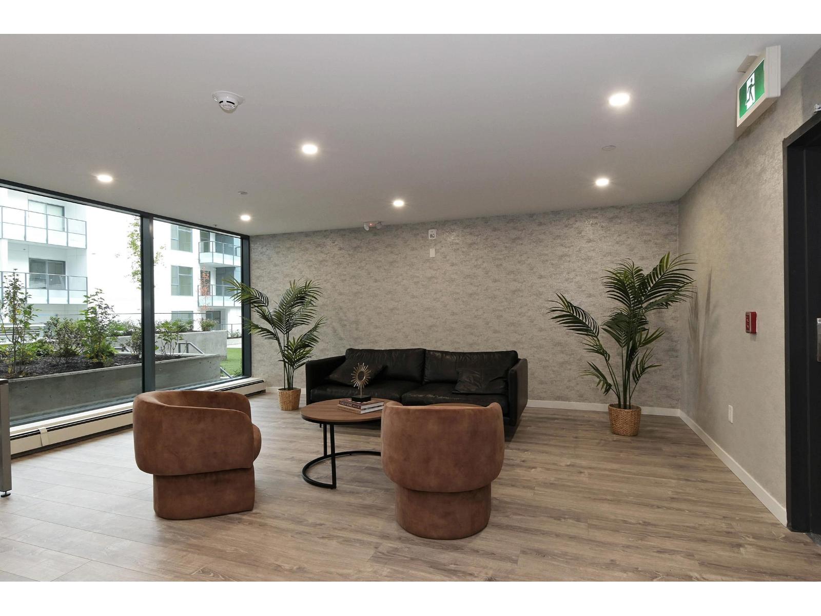A living room with a black couch, two brown ottomans, and a fire extinguisher on the wall.