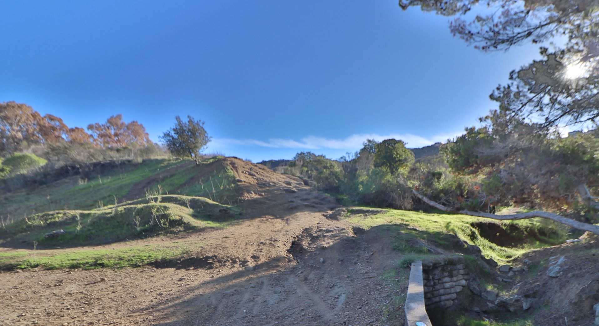 a dirt road leading up a hill with trees and a bridge
