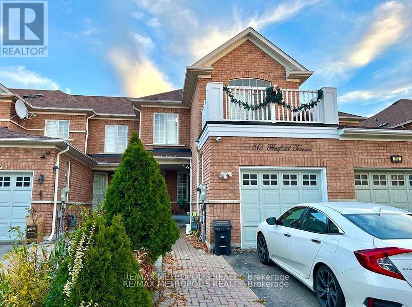 A white car is parked in front of a brick house with a balcony.