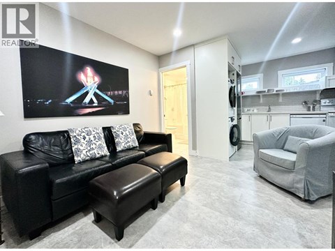 A living room with a black couch and a painting of a firework on the wall.