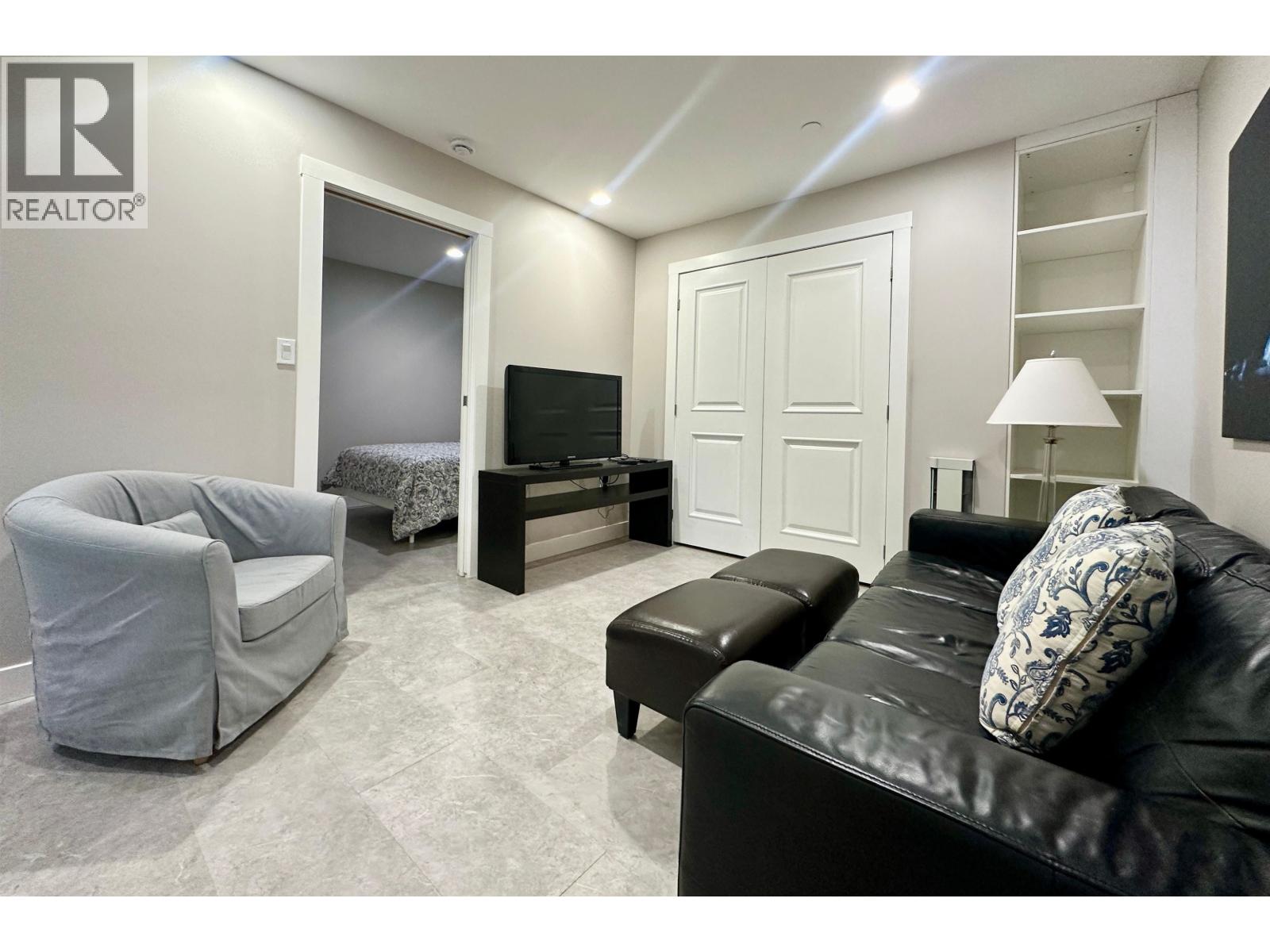 A living room with a grey couch, a black ottoman, and a television.
