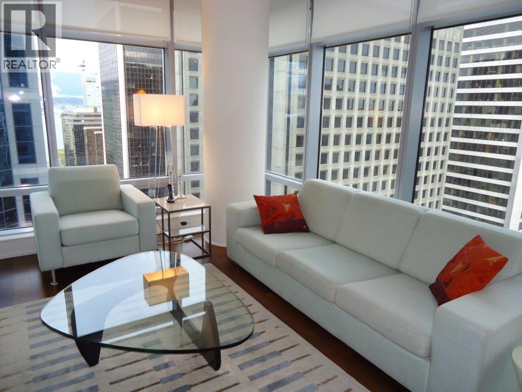 A living room with a white couch, a glass table, and a lamp.