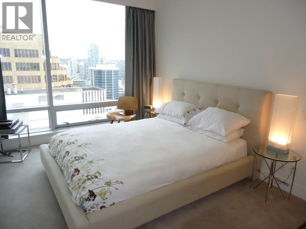 A bedroom with a large bed and a city view through the window.