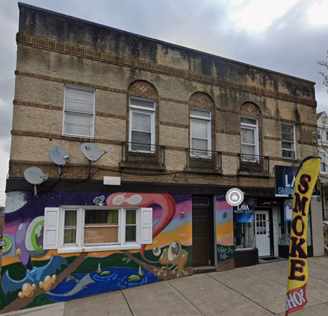 A building with a mural on the side and a sign that says "SMOKE".