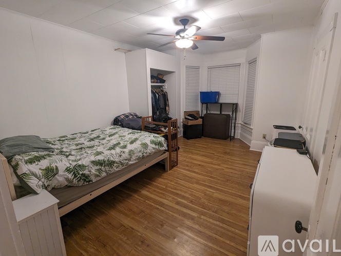 A bedroom with a bed, a ceiling fan, and a wooden floor.