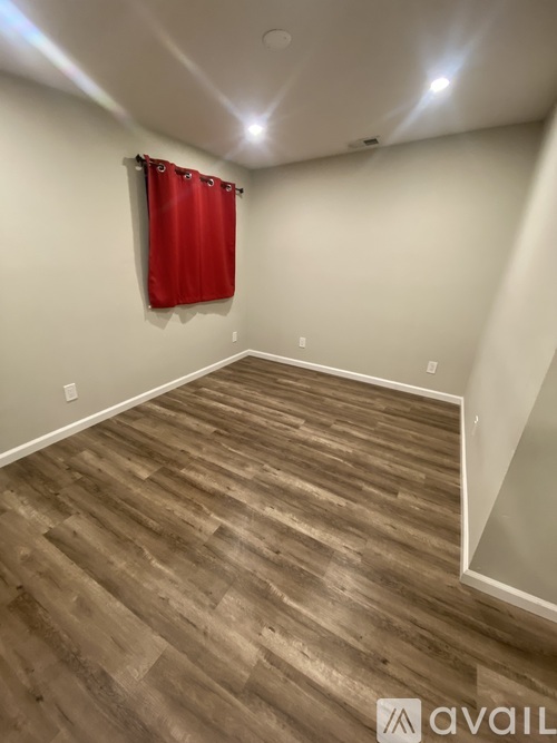 A room with wooden flooring and a red curtain on the window.