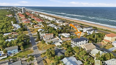 An aerial view of a coastal neighborhood with a prominent orange arrow pointing to a specific house.