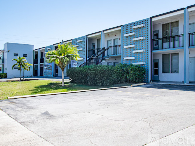 A row of white apartment buildings with balconies and palm trees in front.