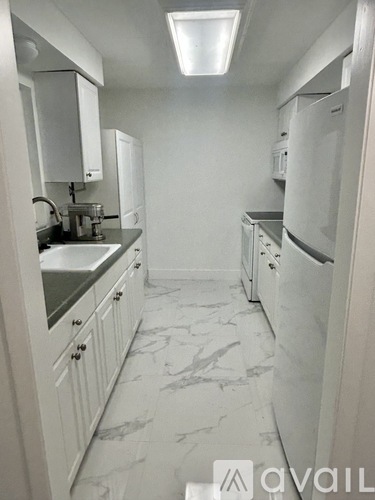 A kitchen with white cabinets and marble flooring.