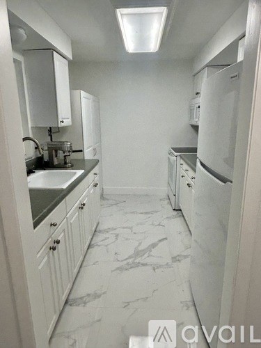 A kitchen with white cabinets and marble flooring.