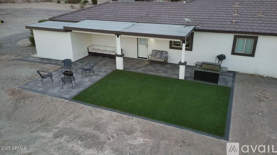 A house with a white exterior and a brown roof has a patio with a table and chairs.