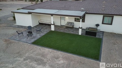 A house with a white exterior and a brown roof has a patio with a table and chairs.
