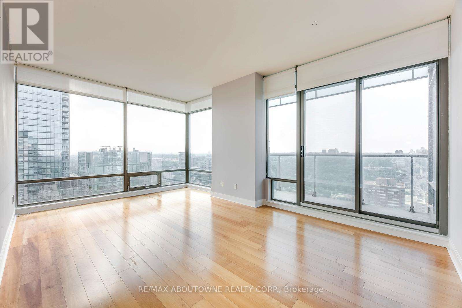 A spacious room with wooden floors and large windows overlooking a cityscape.