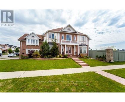 A large, two-story house with a well-manicured lawn and a stone pillar in the front yard.