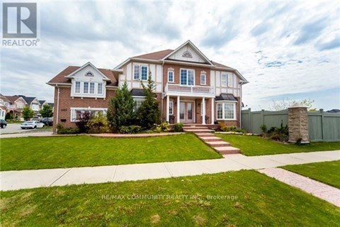 A large, two-story house with a well-manicured lawn and a stone pillar in the front yard.