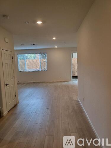A room with wooden floors and white walls, with a window and a door visible.