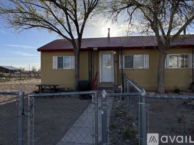 A small house with a red roof and a fence in front of it.