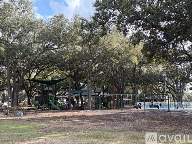 A playground with a green slide and a fence is surrounded by trees.