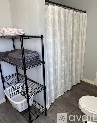 A bathroom with a white shower curtain and a black shelf with towels and a basket.