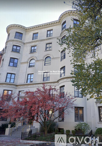 A large white building with a curved corner and a tree with red leaves in front.