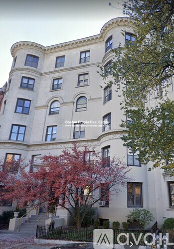 A large white building with a curved corner and a tree with red leaves in front.