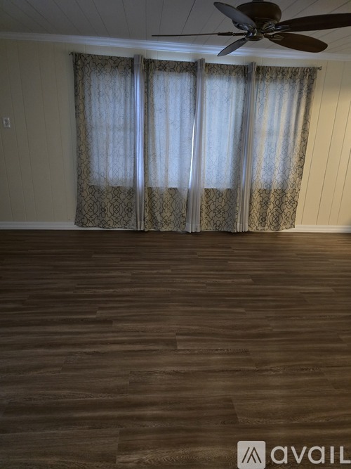 A room with a ceiling fan and a window with curtains.