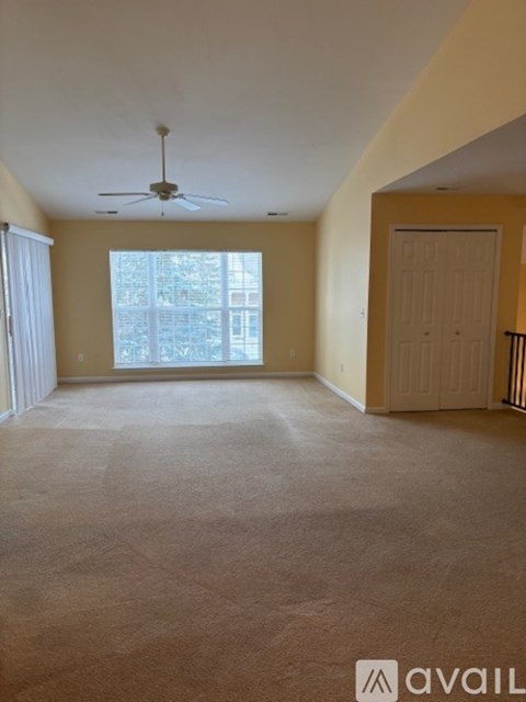 A room with a carpeted floor, a ceiling fan, and a sliding glass door.