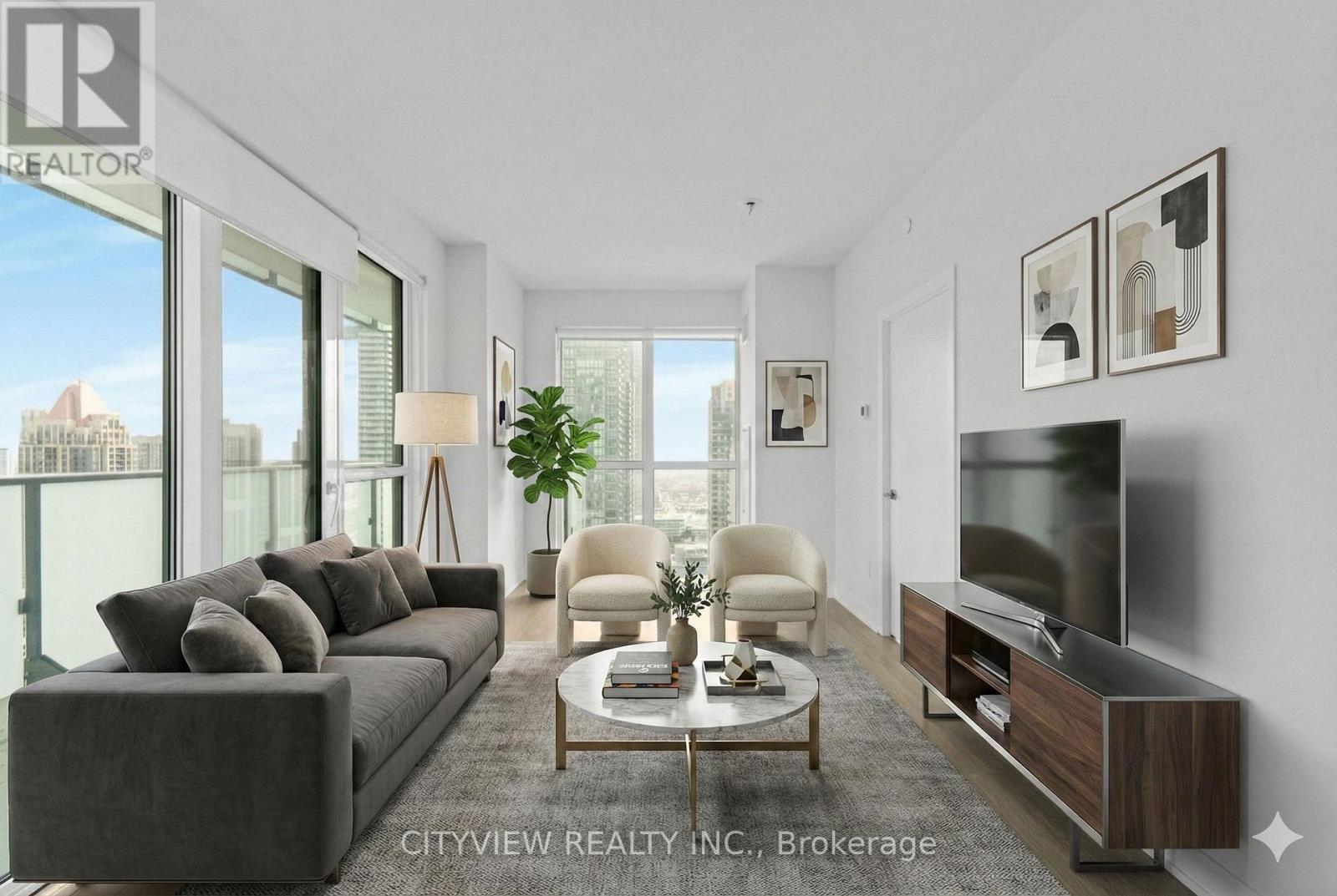 A living room with a grey couch, a white chair, a wooden coffee table, and a flat screen TV mounted on the wall.
