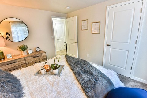 A bedroom with a grey and white rug, a round mirror, and a wooden dresser.
