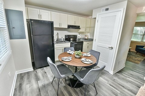 A kitchen with a black refrigerator and a dining table with four chairs.