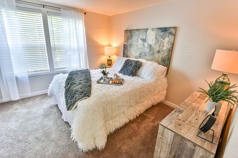 A bedroom with a white bed and a wooden nightstand.