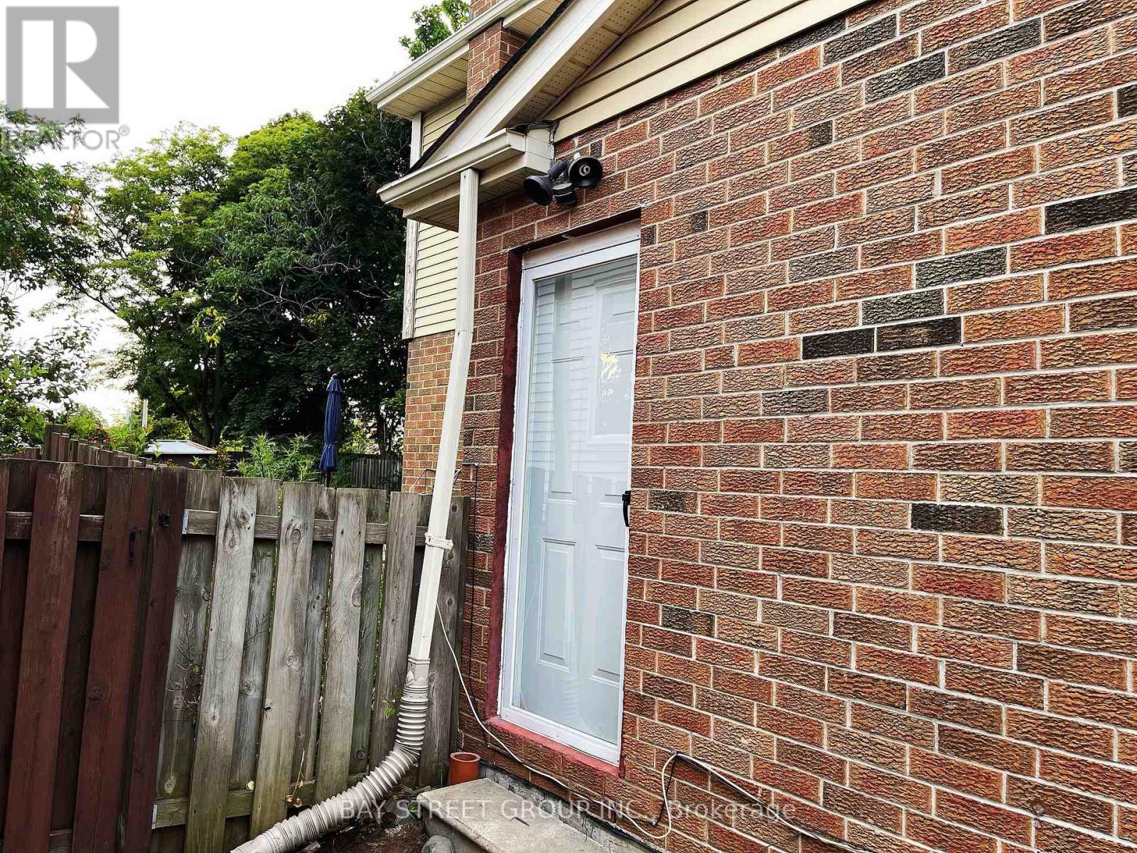 A red brick house with a white door and a white pipe coming out of the ground.