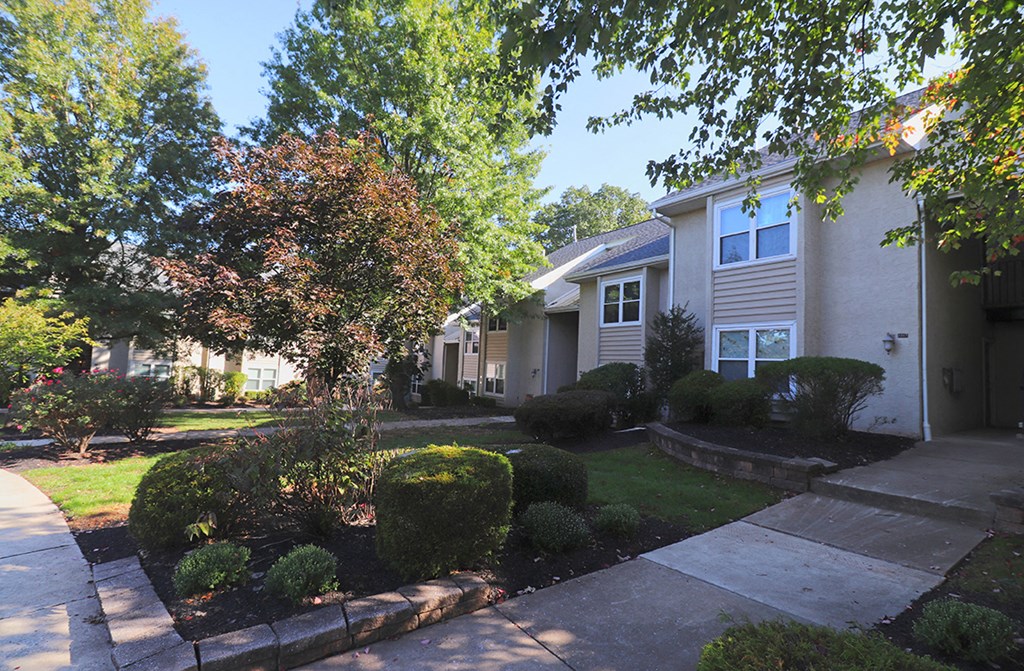 a sidewalk in front of a white house with trees and bushes