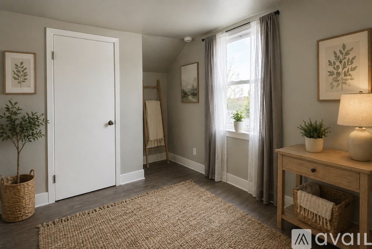 A room with a white door, a window with curtains, and a wooden table with a lamp and a plant on it.