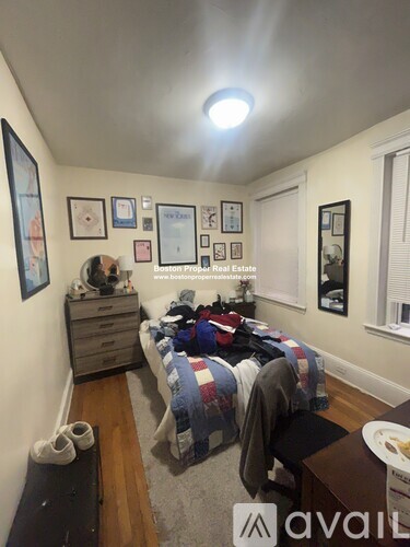 A bedroom with a bed, dresser, and a wall with pictures and a sign that says "Boston Real Estate".