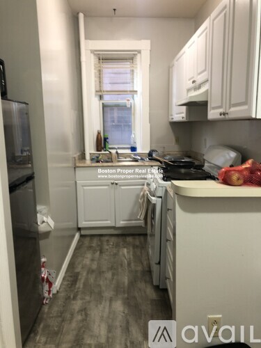 A kitchen with a refrigerator on the left and a window above the sink.