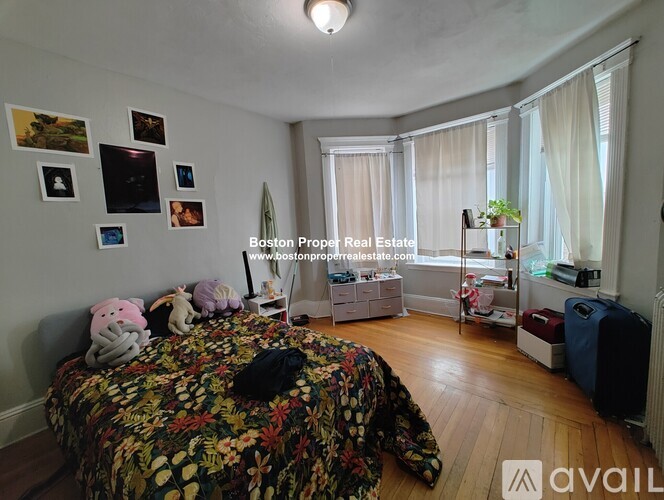 A bedroom with a bed, a window with curtains, and a wall with pictures.