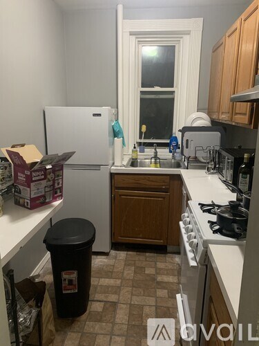 A kitchen with a white fridge, brown cabinets, and a black trash can.